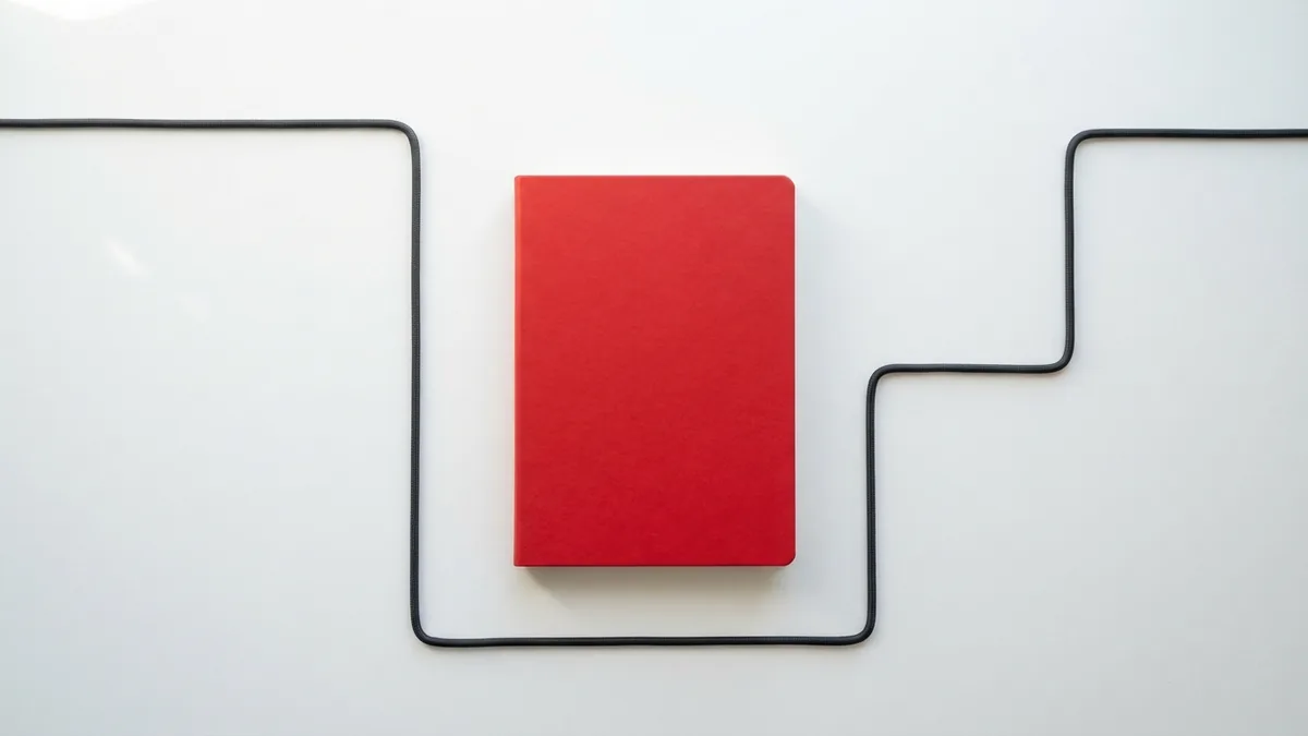 Crimson notebook and black cable arranged on a white desk for setup steps
